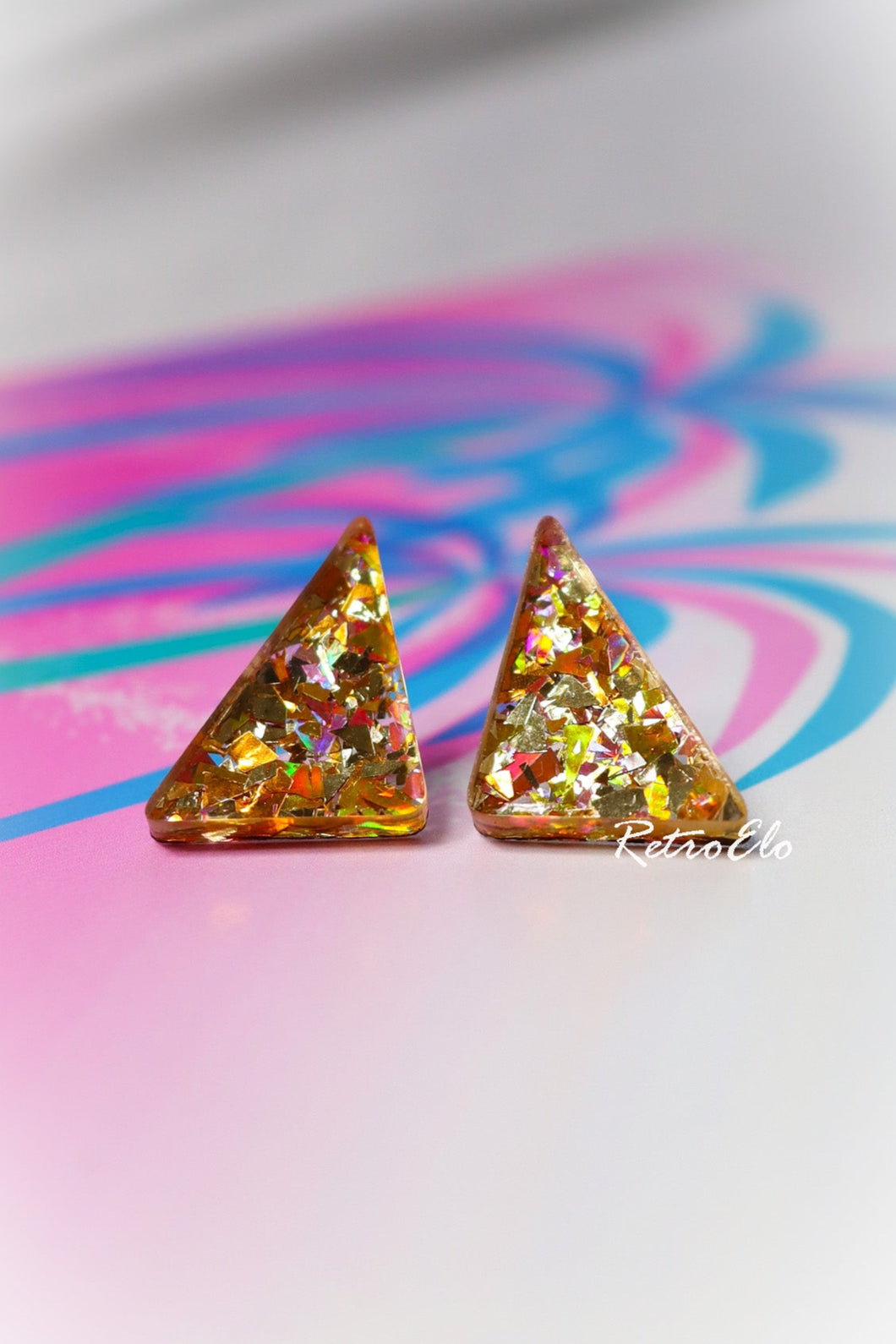 Triangular glittery earrings on a colorful abstract background